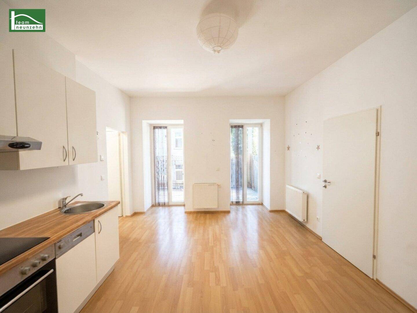 Heller Wohnbereich mit integrierter Küchenzeile, Holzboden und zwei französischen Balkonen.