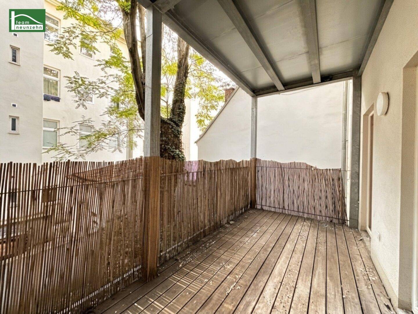 Ruhiger Balkon mit Holzboden und Bambusverkleidung, umgeben von städtischer Bebauung.