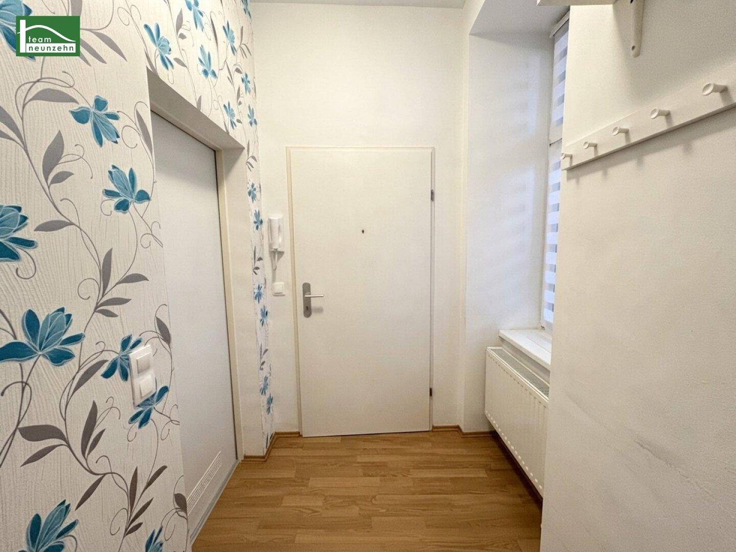 Eingangsbereich mit floraler Tapete, Garderobe und Holzboden, hell und einladend gestaltet.