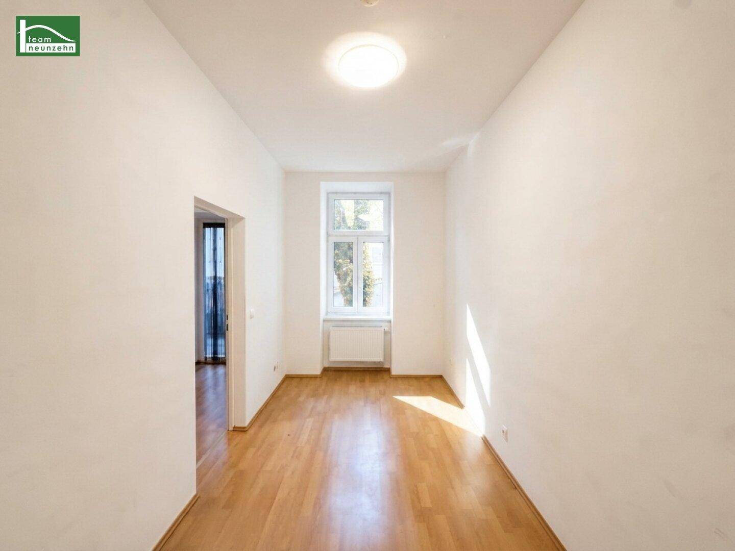 Helles Zimmer mit Holzboden und großem Fenster, das viel natürliches Licht hereinlässt.