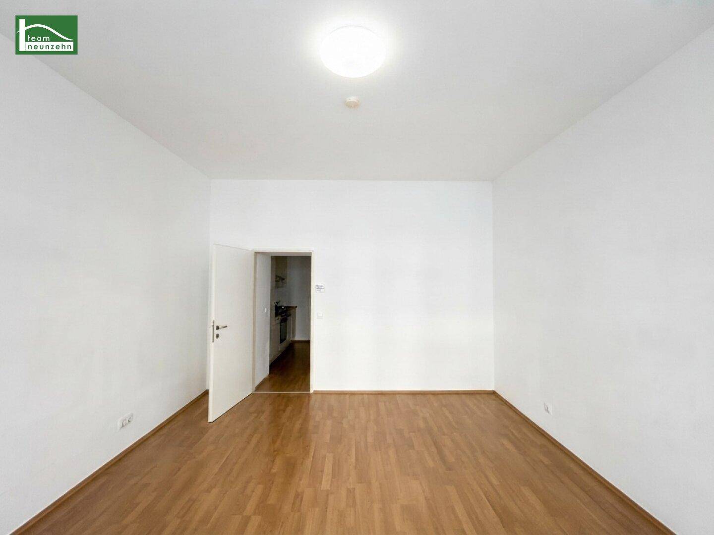 Geräumiges, leeres Zimmer mit Parkettboden und offener Tür zu einem weiteren Bereich.