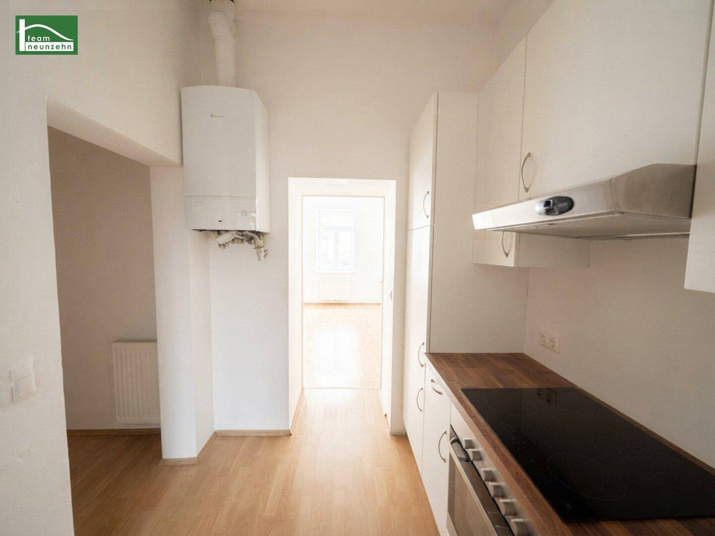 Funktionale Küche mit weißen Schränken, Holz-Arbeitsplatte und Blick in einen weiteren Raum.