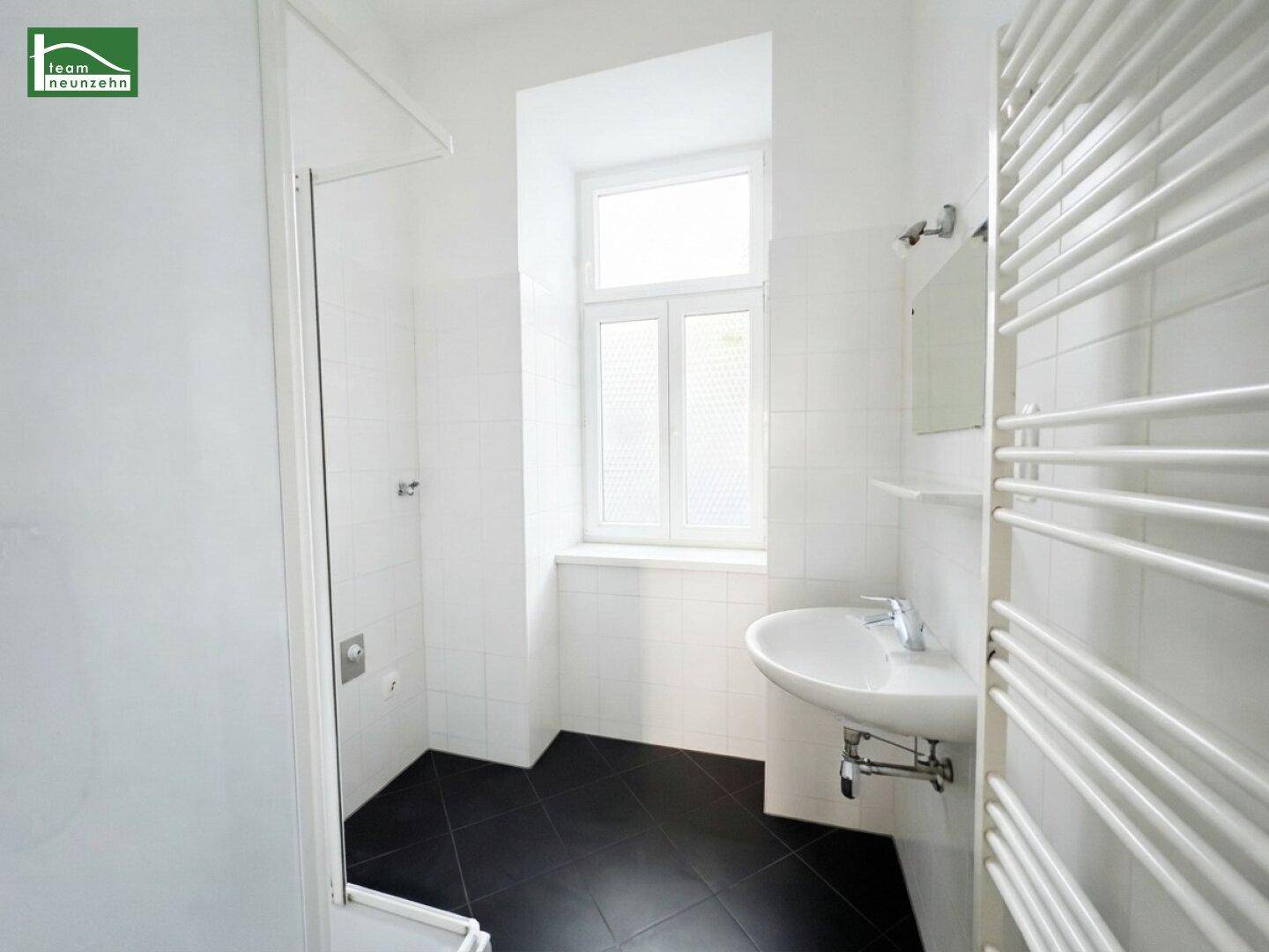 Modernes Badezimmer mit Dusche, Waschbecken, Fenster und dunklen Bodenfliesen.