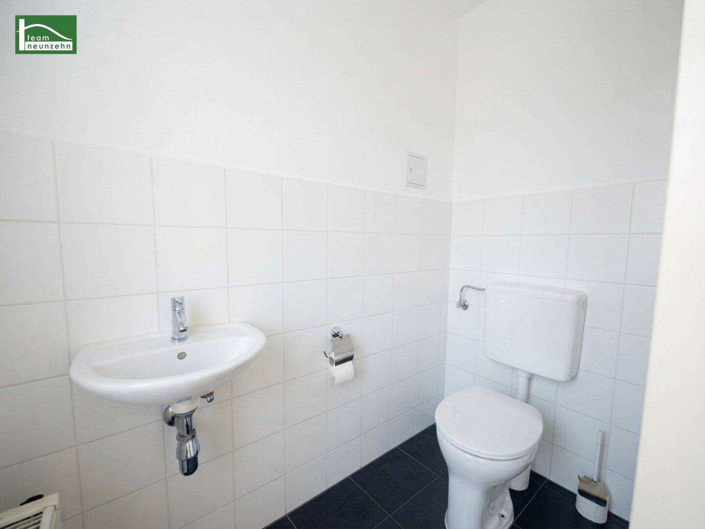 Separates WC mit Waschbecken, Toilette und weißen Fliesen, ideal für Gäste.