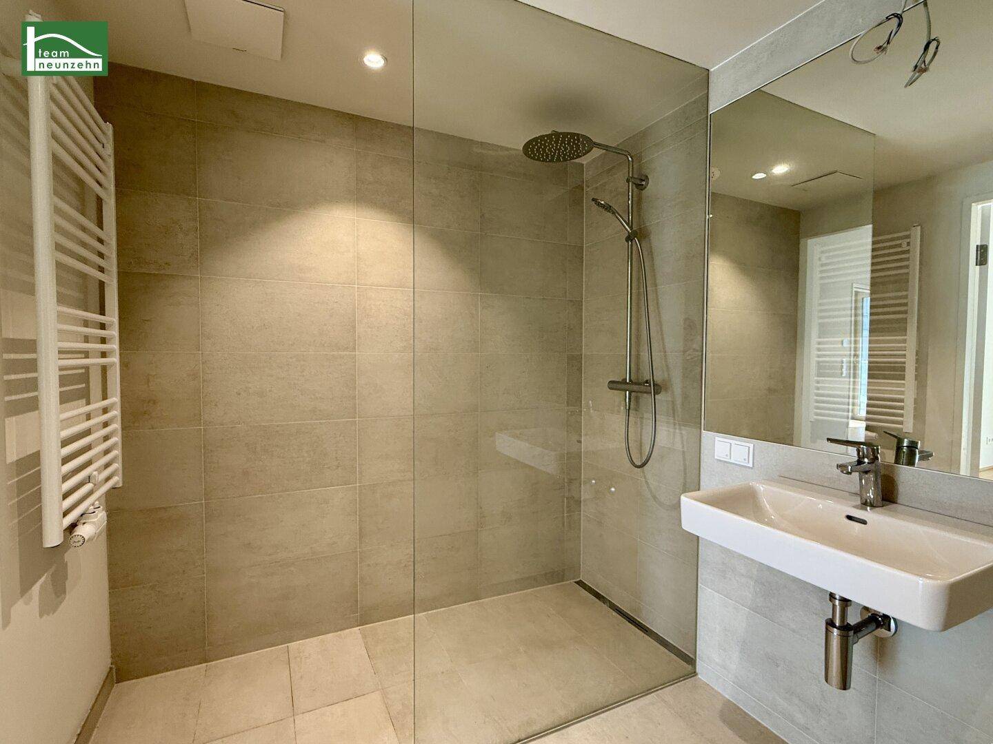 Modernes Badezimmer mit ebenerdiger Dusche, großformatigen Fliesen und Handtuchheizkörper.
