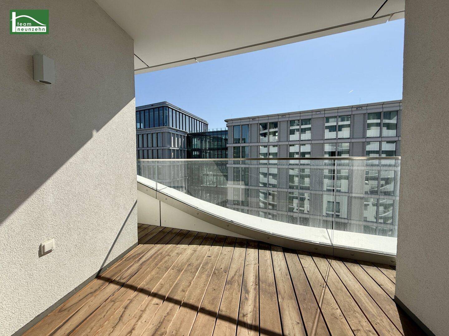 Moderner Balkon mit Holzboden und Glasbrüstung, bietet einen Blick auf die Stadt.