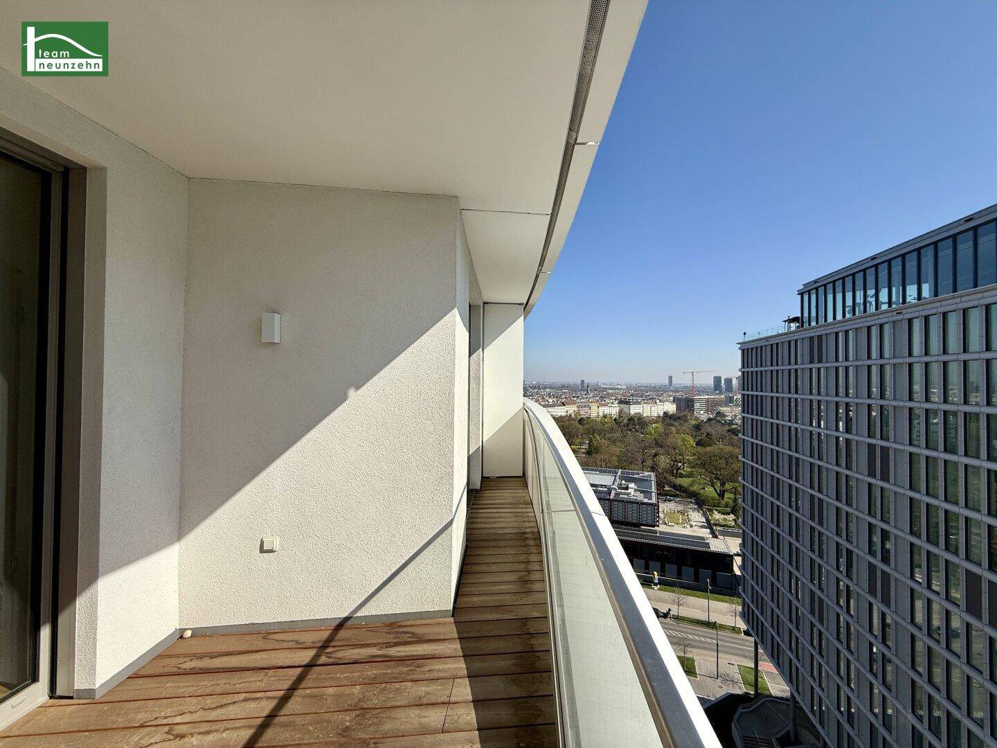 Langer Balkon mit Holzboden und Glasgeländer, bietet weitreichenden Stadtblick.
