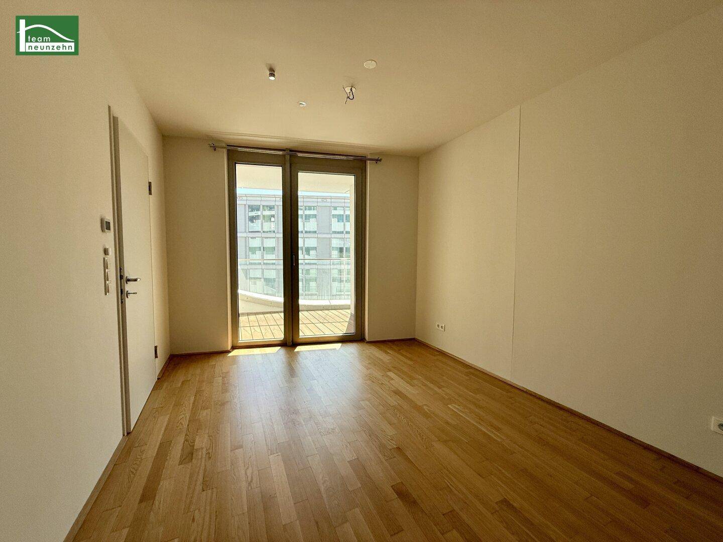 Helles Schlafzimmer mit Holzboden und großen Fenstern, die viel Tageslicht hereinlassen.