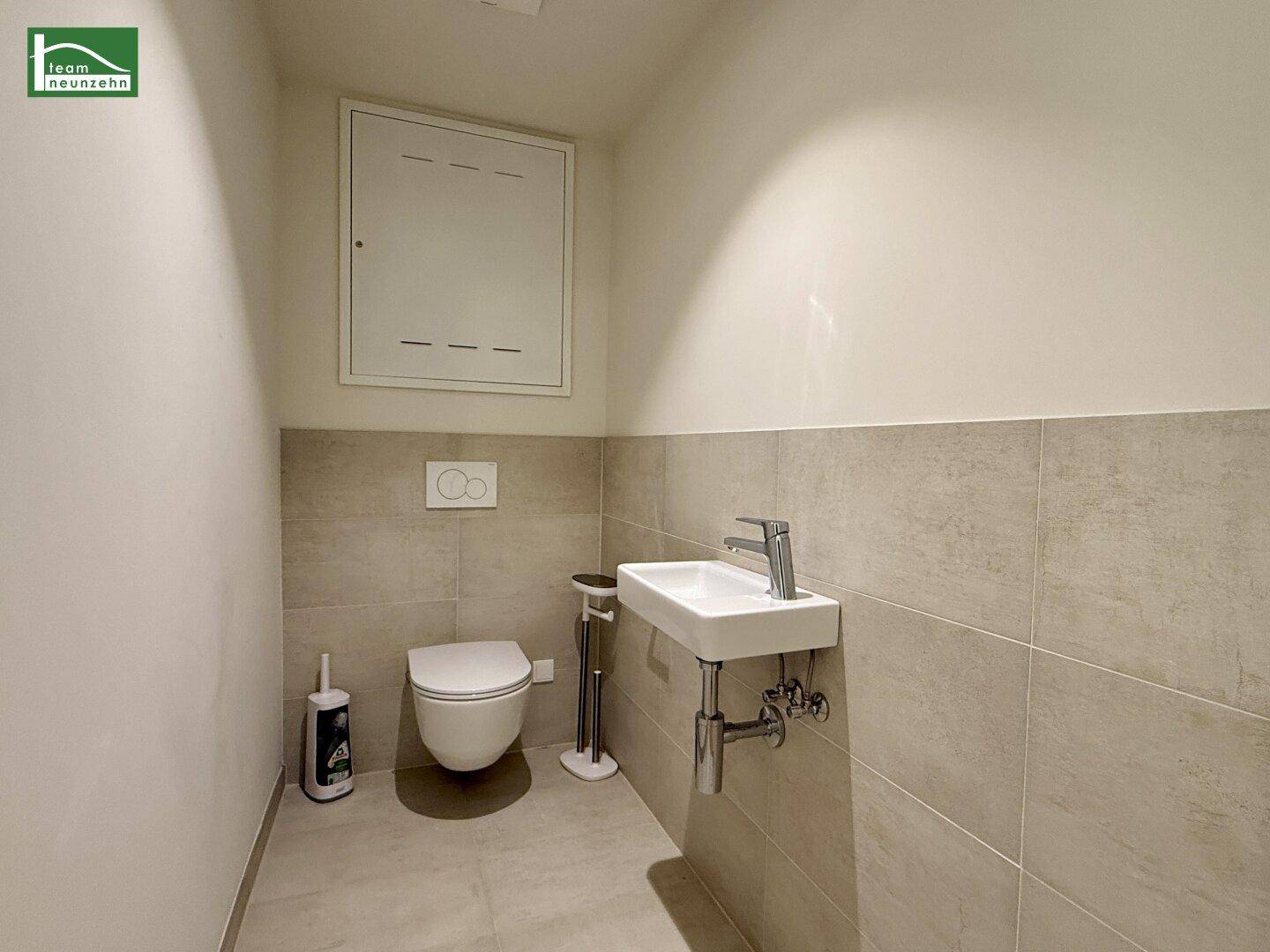 Separate Gästetoilette mit Wand-WC, kleinem Waschbecken und modernen Fliesen.