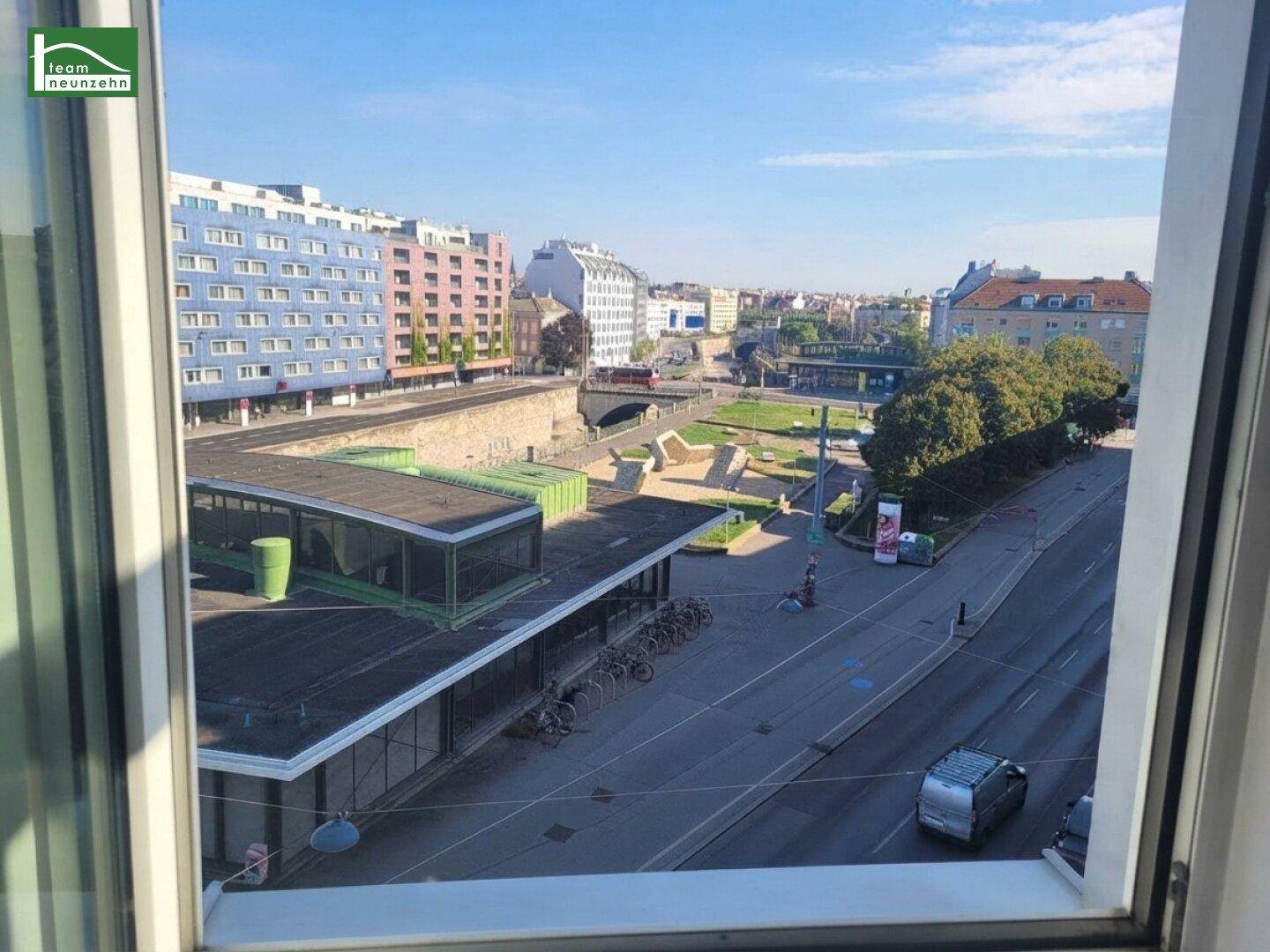 Heller Ausblick aus einem Fenster auf eine belebte Stadtlandschaft mit Gebäuden und Grünflächen.