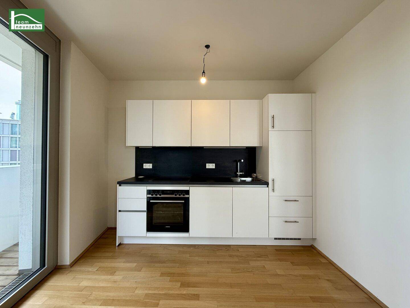 Moderne Küchenzeile mit weißen Schränken, schwarzer Arbeitsplatte und integriertem Backofen.