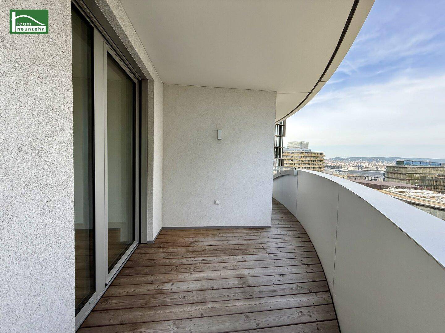 Geschwungener Balkon mit Holzbelag und weitem Blick über die Stadtlandschaft.
