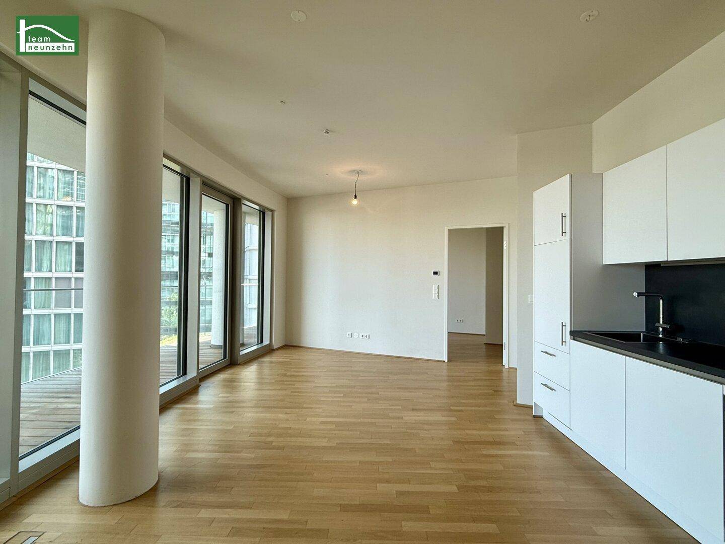 Geräumiger offener Wohnbereich mit Parkettboden und Zugang zum Balkon durch große Fenster.