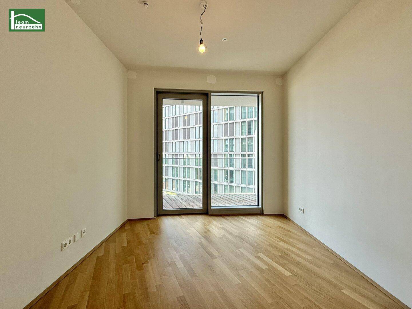 Helles Schlafzimmer mit Parkettboden und großem Fenster mit Zugang zum Balkon.