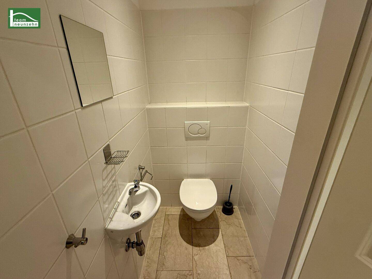 Kleines Gäste-WC mit Wand-WC, Waschbecken und weißen Fliesen.