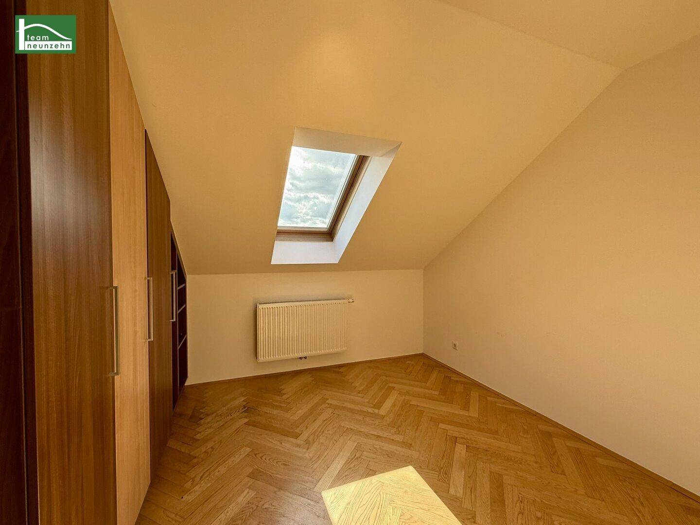 Schlafzimmer mit Holzschrank, Fischgrätparkett und Dachfenster für natürliches Licht.