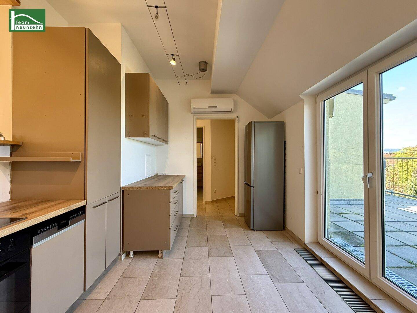 Funktionale Küche mit Fliesenboden, Kühlschrank und Klimaanlage sowie Terrassenzugang.