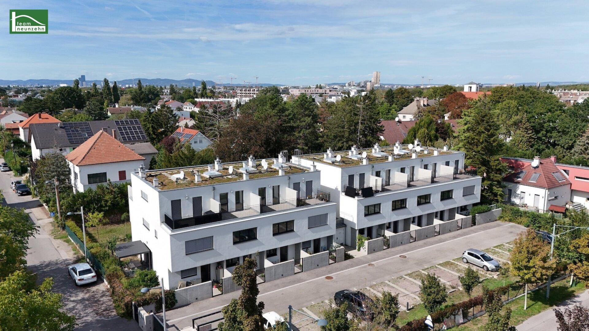 Moderne Reihenhäuser mit weißer Fassade und begrünten Dächern, umgeben von viel Grün und Wohnbebauung.