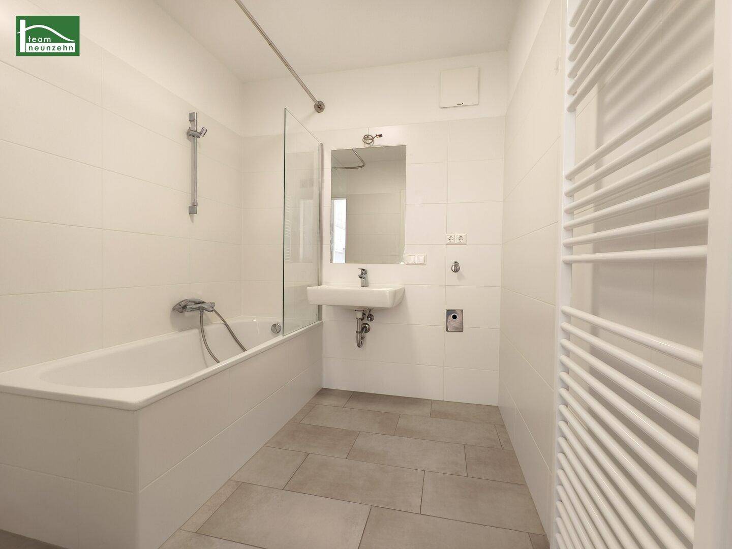 Modernes Badezimmer mit Badewanne, Einzelwaschbecken und beheiztem Handtuchhalter.