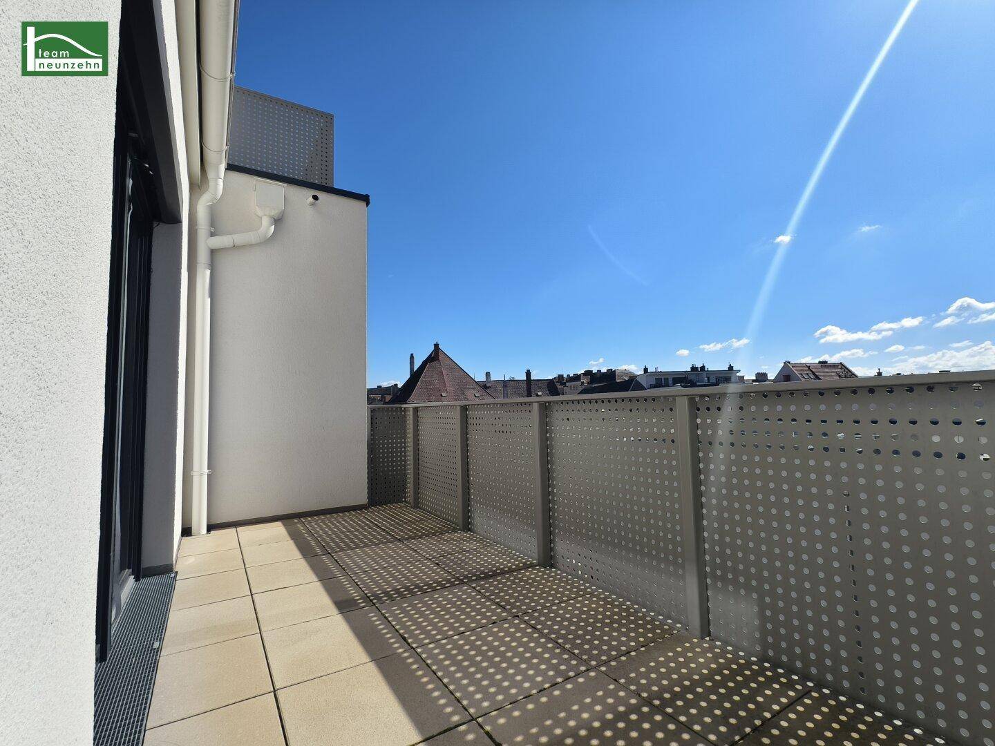 Sonniger Balkon mit Fliesenboden und moderner Metallbrüstung, bietet einen Blick über die Dächer.