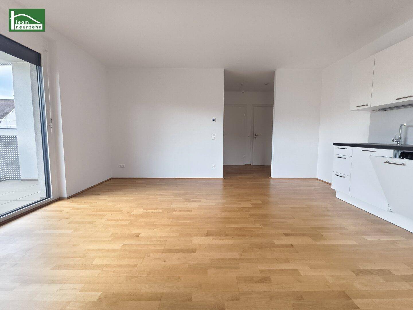 Lichtdurchfluteter Wohnbereich mit Zugang zum Balkon und hellem Holzboden.