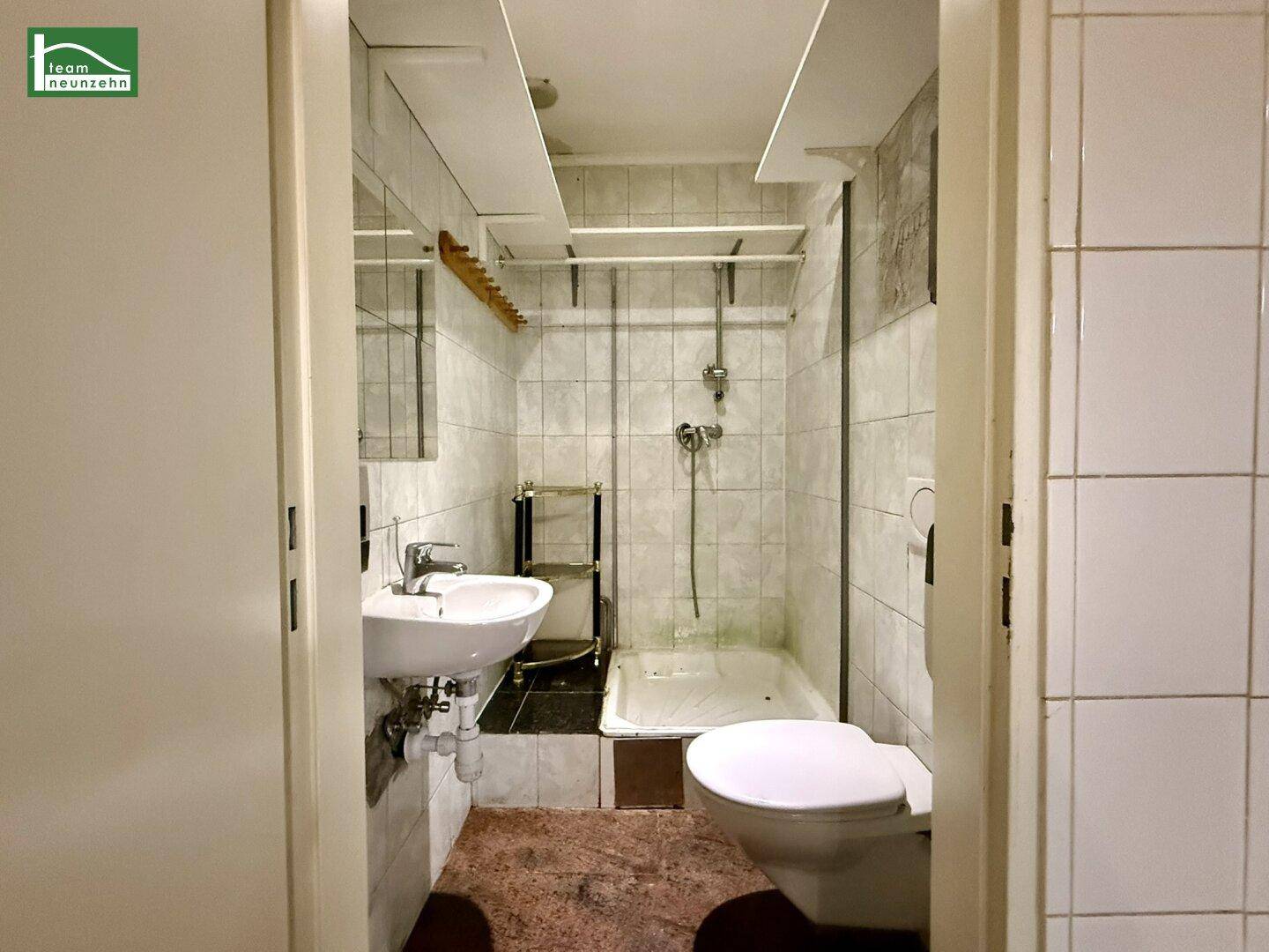 Kleines Badezimmer mit Dusche, Waschbecken und Toilette, komplett gefliest und funktional eingerichtet.