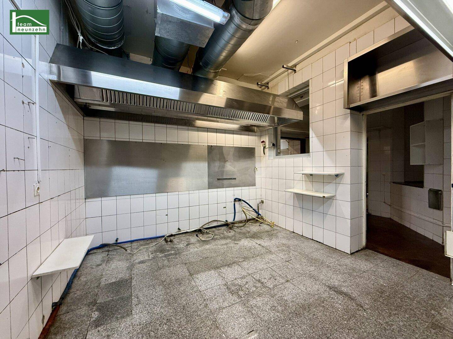 Geräumige Gewerbeküche mit Fliesenwänden, großen Ablufthauben und einem Fenster für natürliche Belüftung.