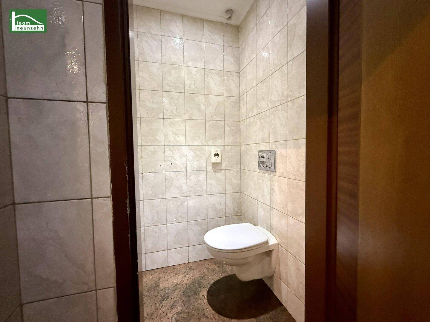Einfaches Gäste-WC mit gefliesten Wänden und wandhängender Toilette, funktional und sauber.