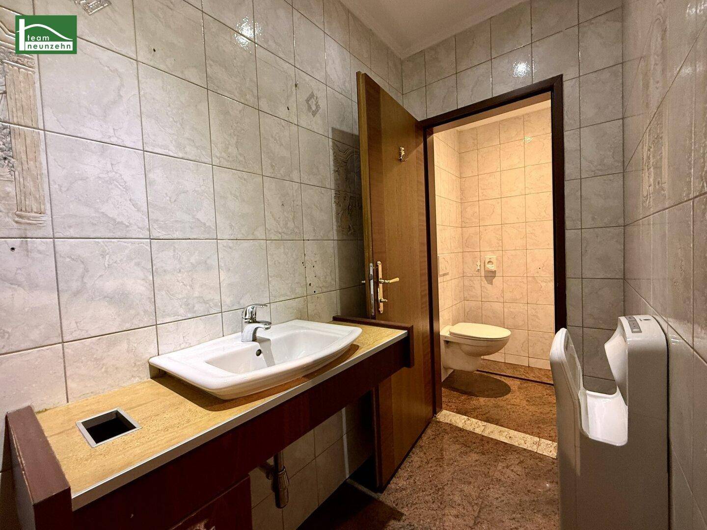 Gefliestes Gäste-WC mit Waschbecken, Spiegel und wandhängender Toilette, ausgestattet mit Handtrockner.