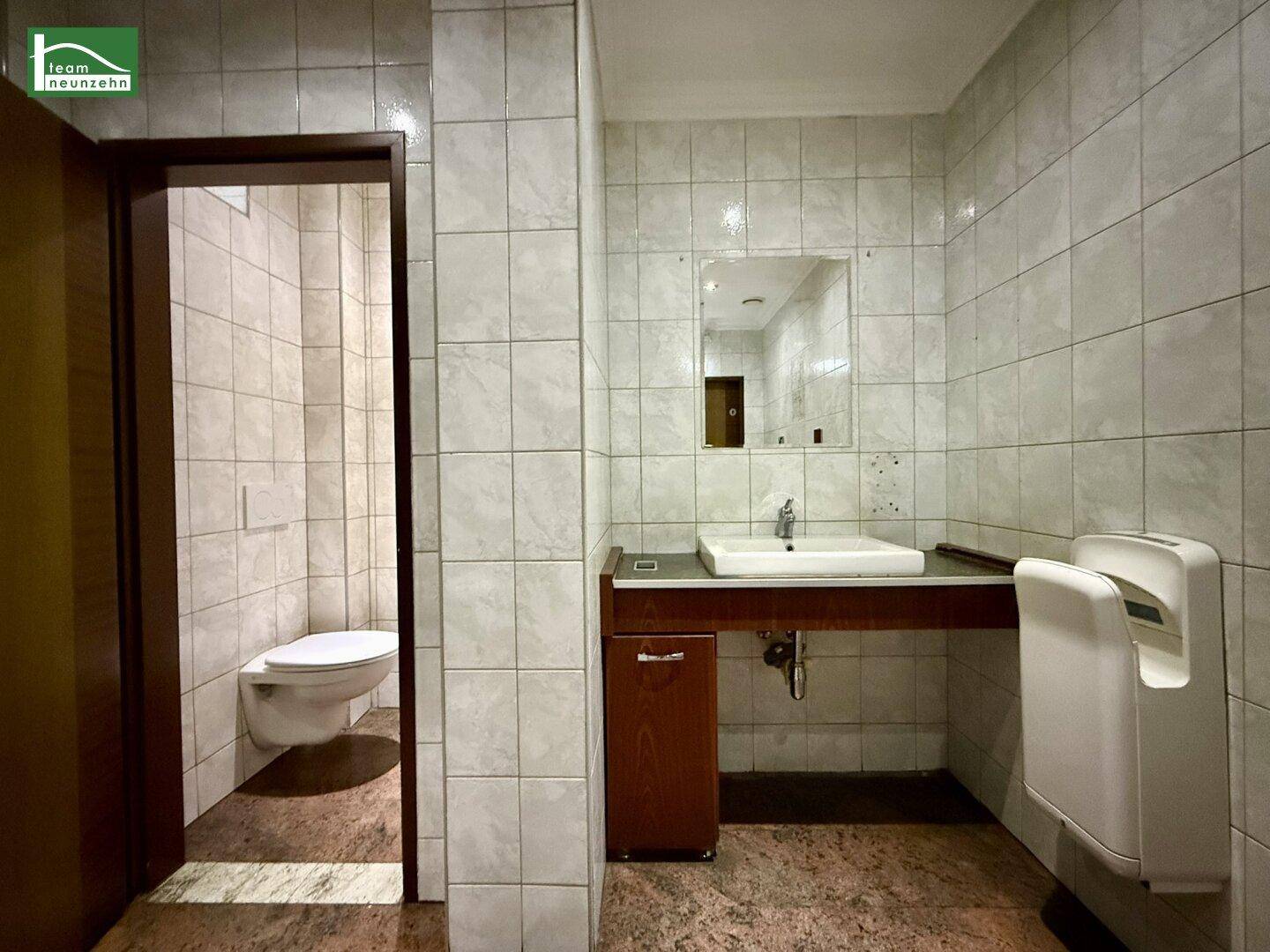 Gefliestes Gäste-WC mit Waschbecken, Spiegel und wandhängender Toilette, ausgestattet mit Handtrockner.