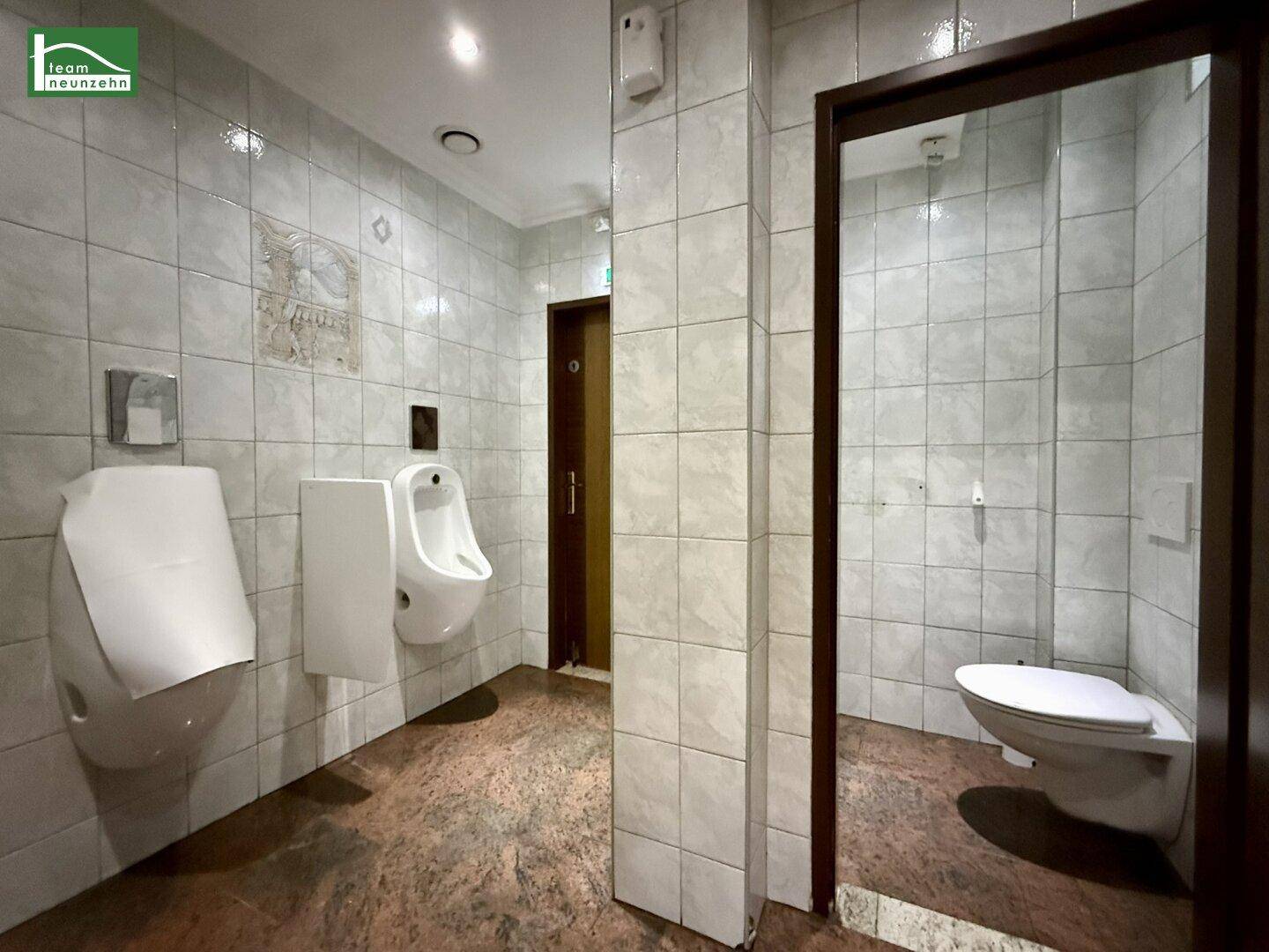 Geräumiges Gäste-WC mit Urinalen, wandhängender Toilette und gefliesten Wänden, funktional und sauber.