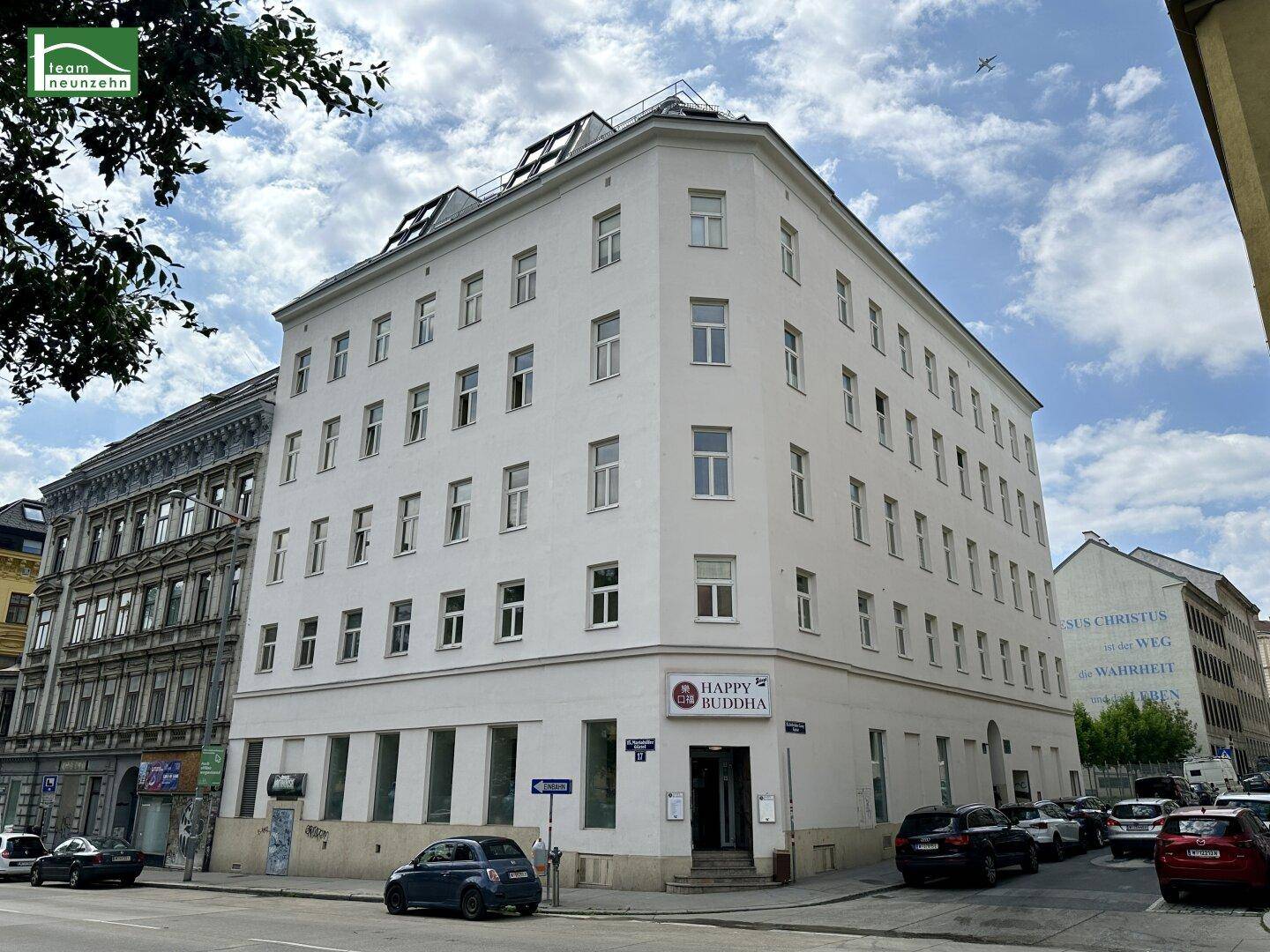 Historisches Eckgebäude mit weißer Fassade und vielen Fenstern in einer städtischen Umgebung.