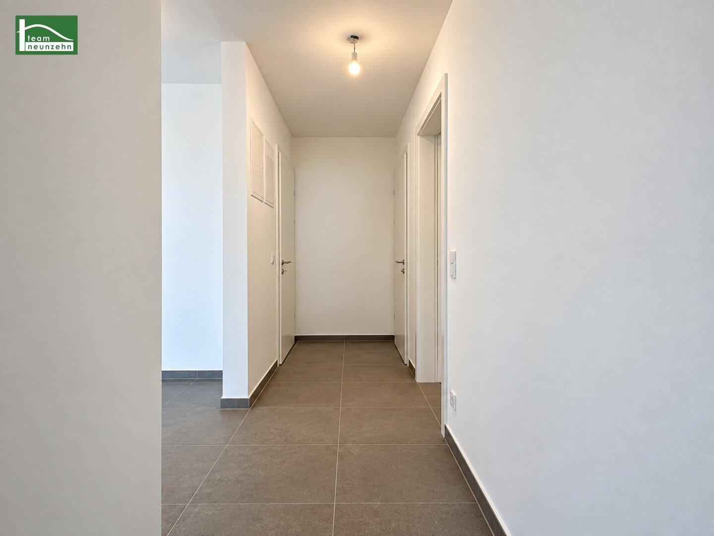 Langer Flur mit Fliesenboden und weißen Wänden, verbindet verschiedene Räume der Wohnung.