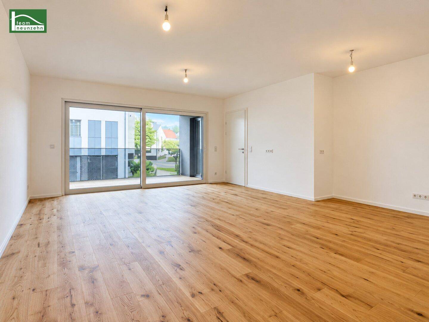 Heller Wohnbereich mit Zugang zu einem Balkon, ausgestattet mit Parkettboden und großen Schiebetüren.