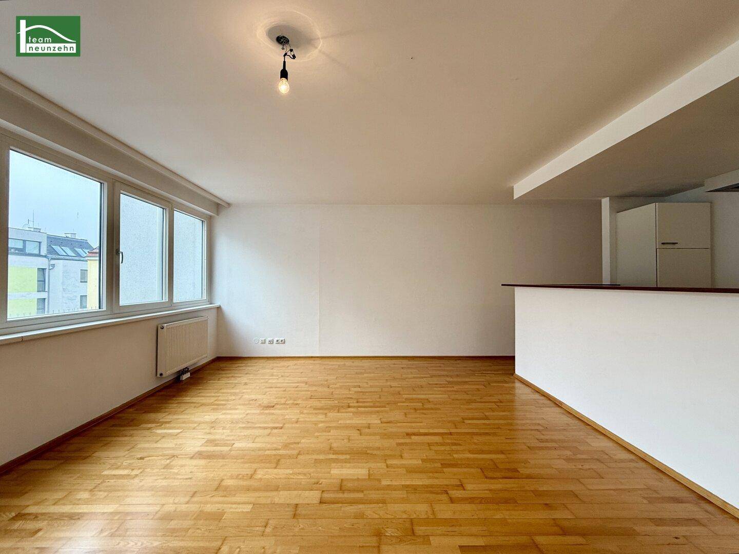 Heller Wohnbereich mit glänzendem Parkettboden und großen Fenstern, die viel Tageslicht hereinlassen.