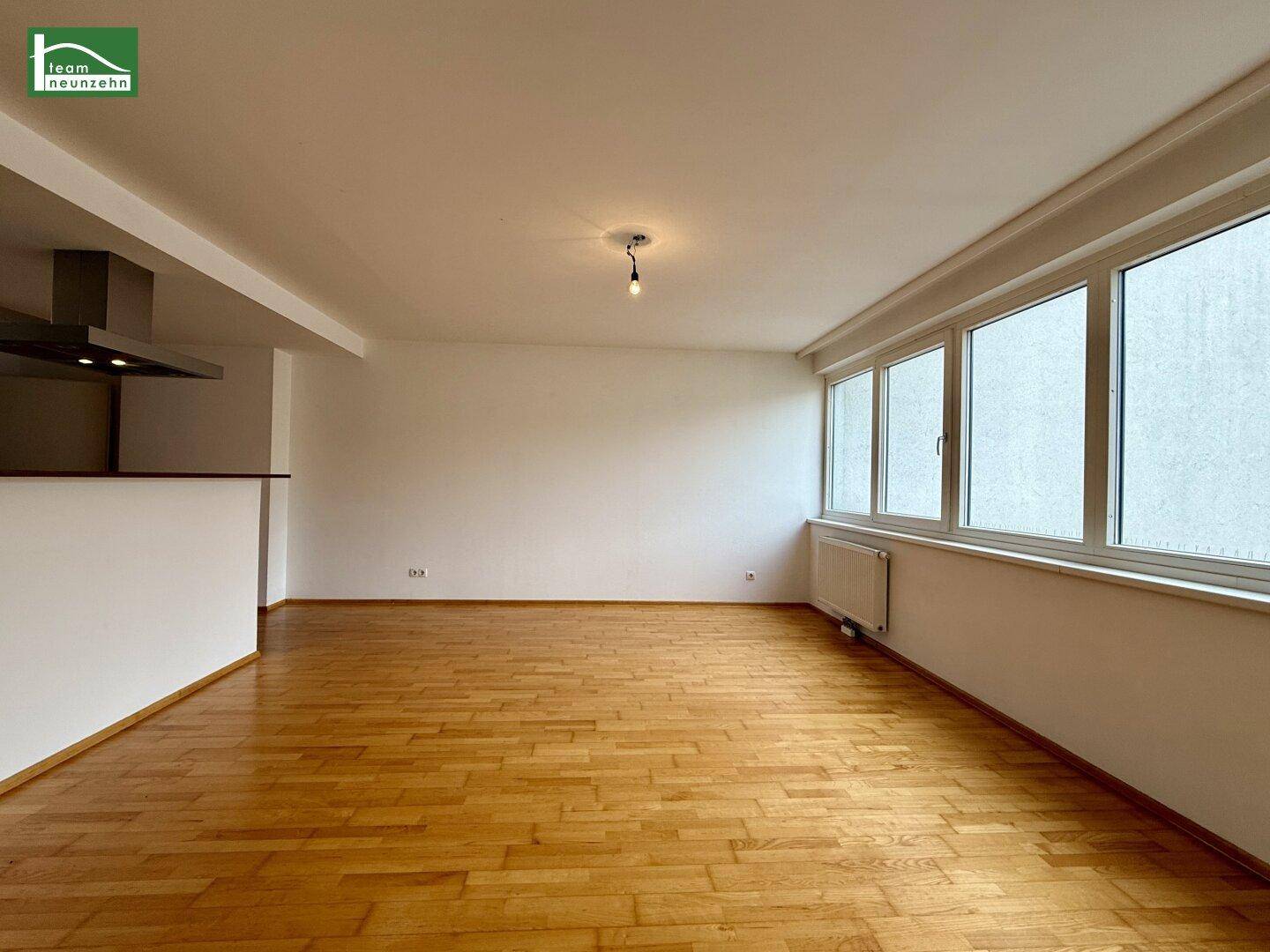 Geräumiger Wohnbereich mit hellem Parkettboden und großen Fenstern für viel Tageslicht.