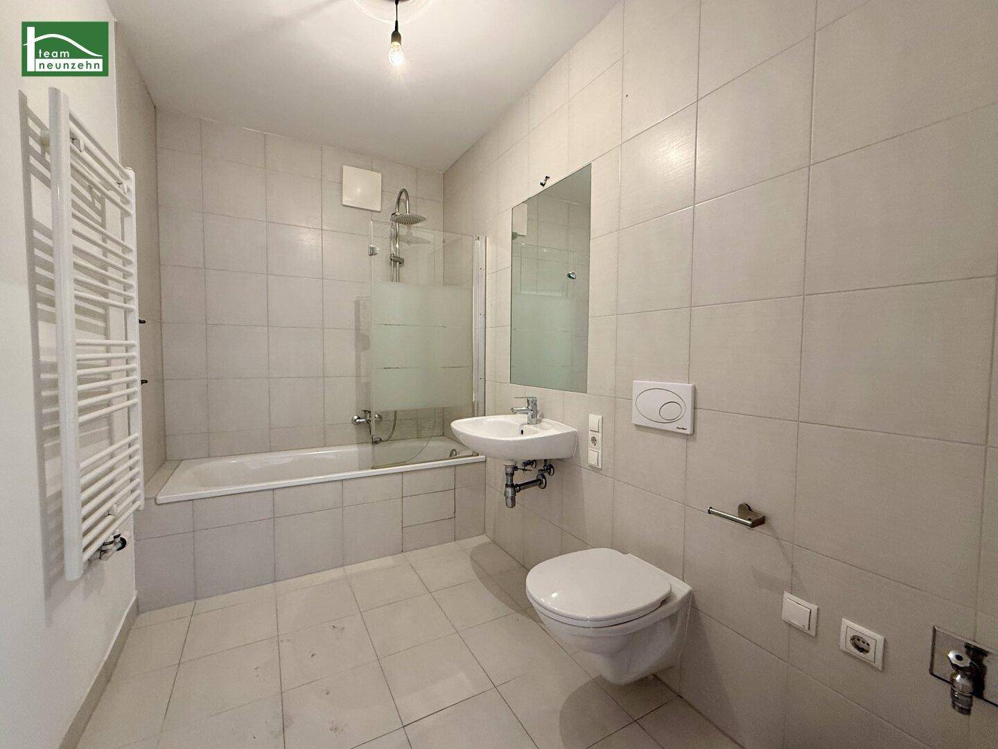 Modernes Badezimmer mit hellen Fliesen, Badewanne mit Duschfunktion und Wand-WC.