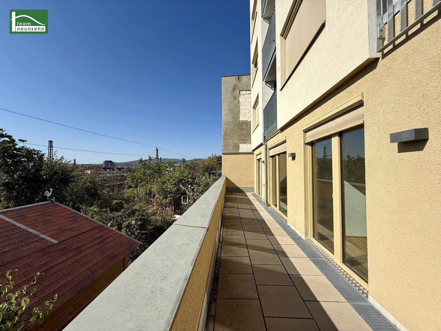 Langer Balkon mit Fliesenboden und Blick auf Bäume sowie die Umgebung.