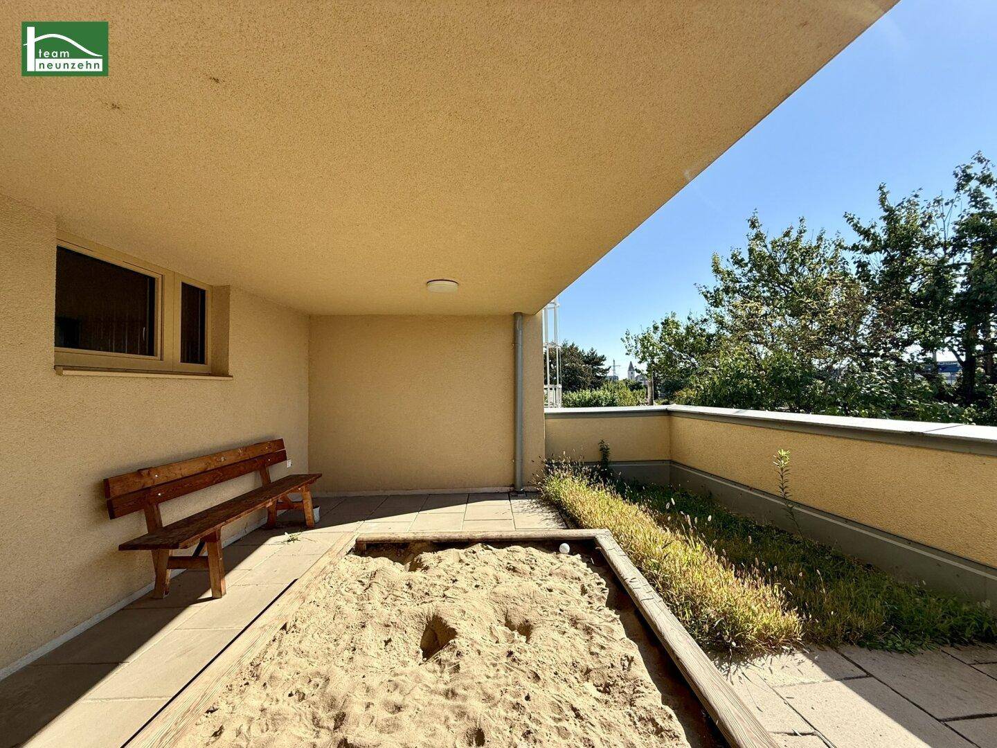 Gemeinschaftlicher Außenbereich mit Sandkasten und Sitzbank, umgeben von Grünflächen.