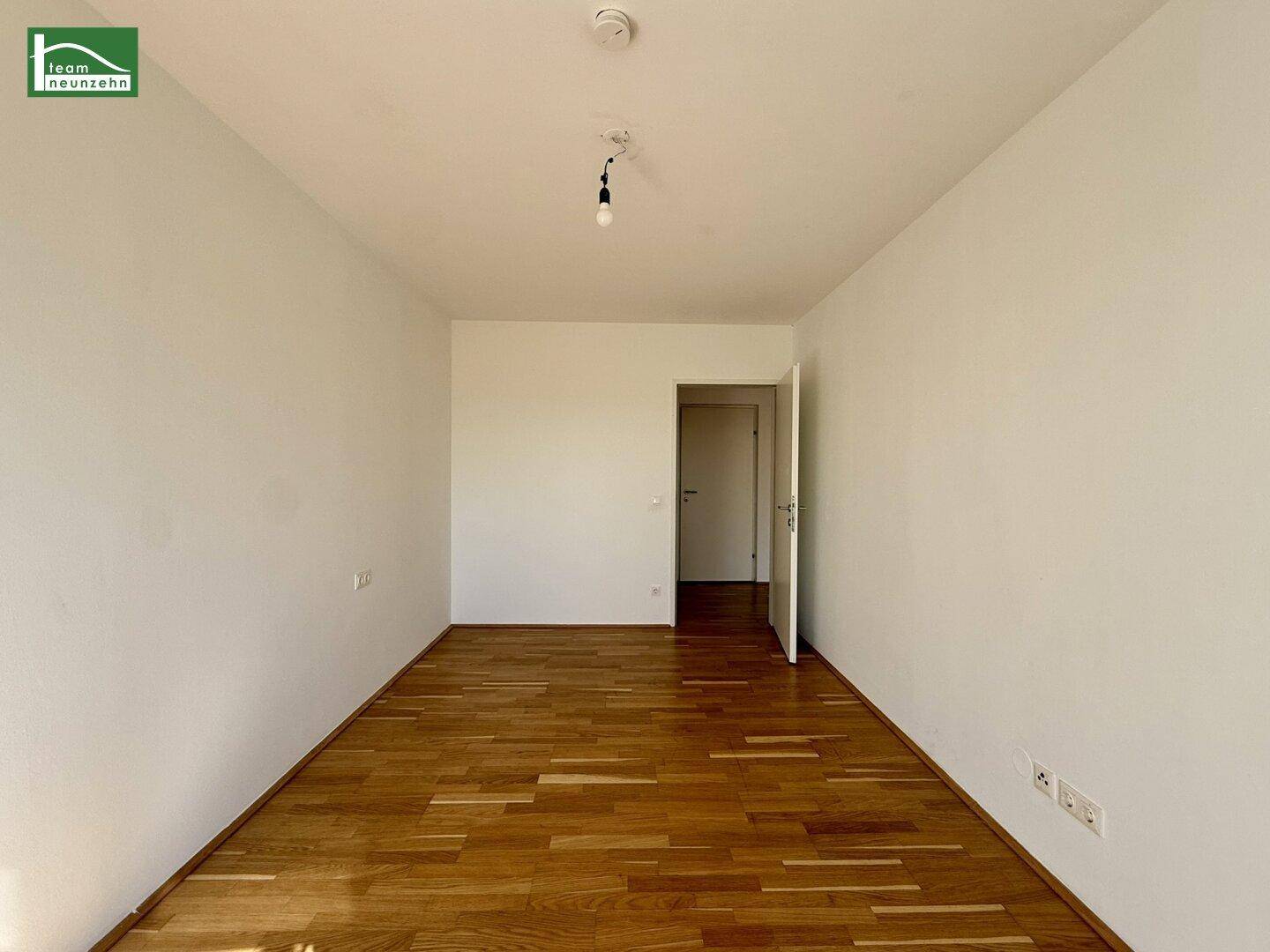 Leeres Zimmer mit Parkettboden und einer Tür, bereit zur individuellen Gestaltung.