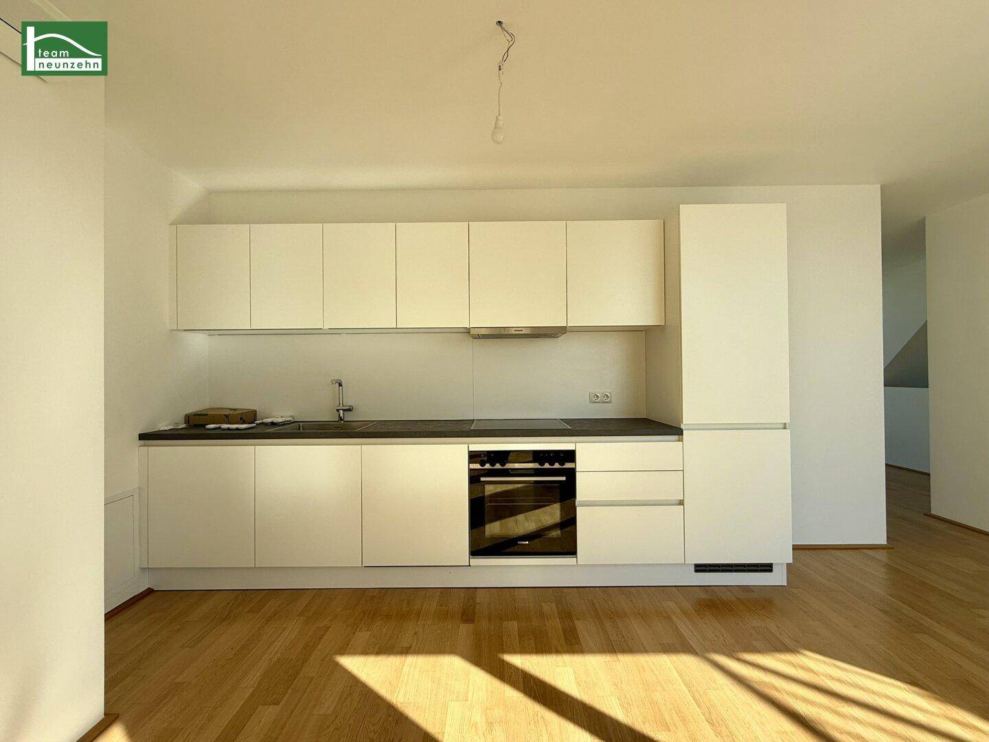 Moderne Einbauküche mit weißen Schränken, dunkler Arbeitsplatte und integrierten Geräten in einem hellen Raum.