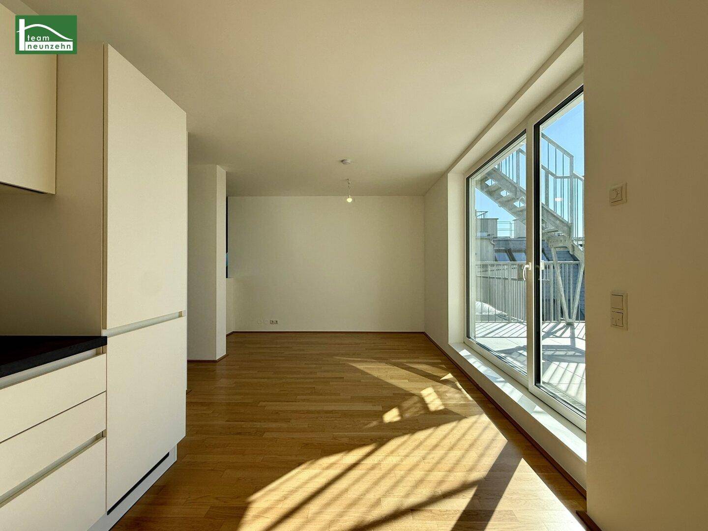 Lichtdurchfluteter Wohnbereich mit Holzboden und großen Fenstern, die Zugang zu einer Außenterrasse bieten.