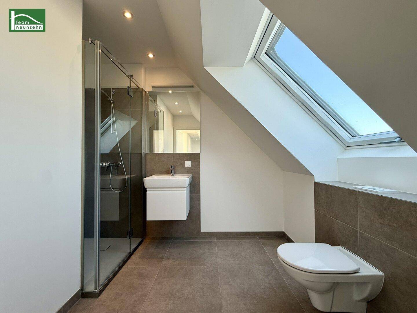 Modernes Badezimmer im Dachgeschoss mit begehbarer Dusche, Wand-WC und Dachfenster für natürliches Licht.