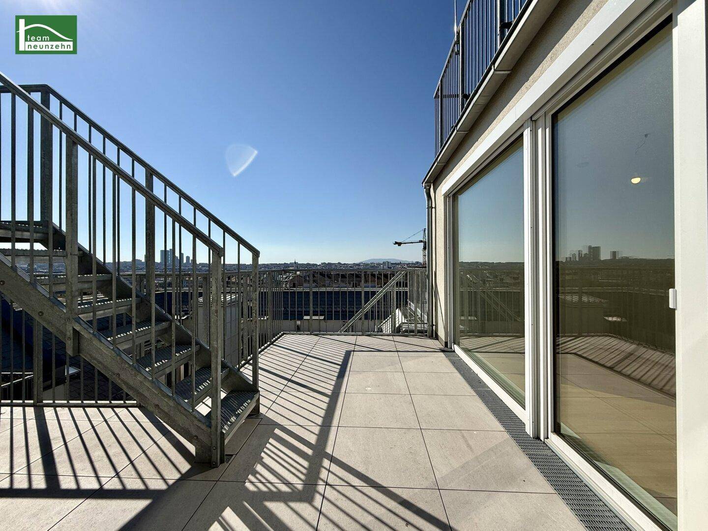 Geräumige Dachterrasse mit Fliesenboden und Metallgeländer, die einen weiten Blick über die Stadt bietet.