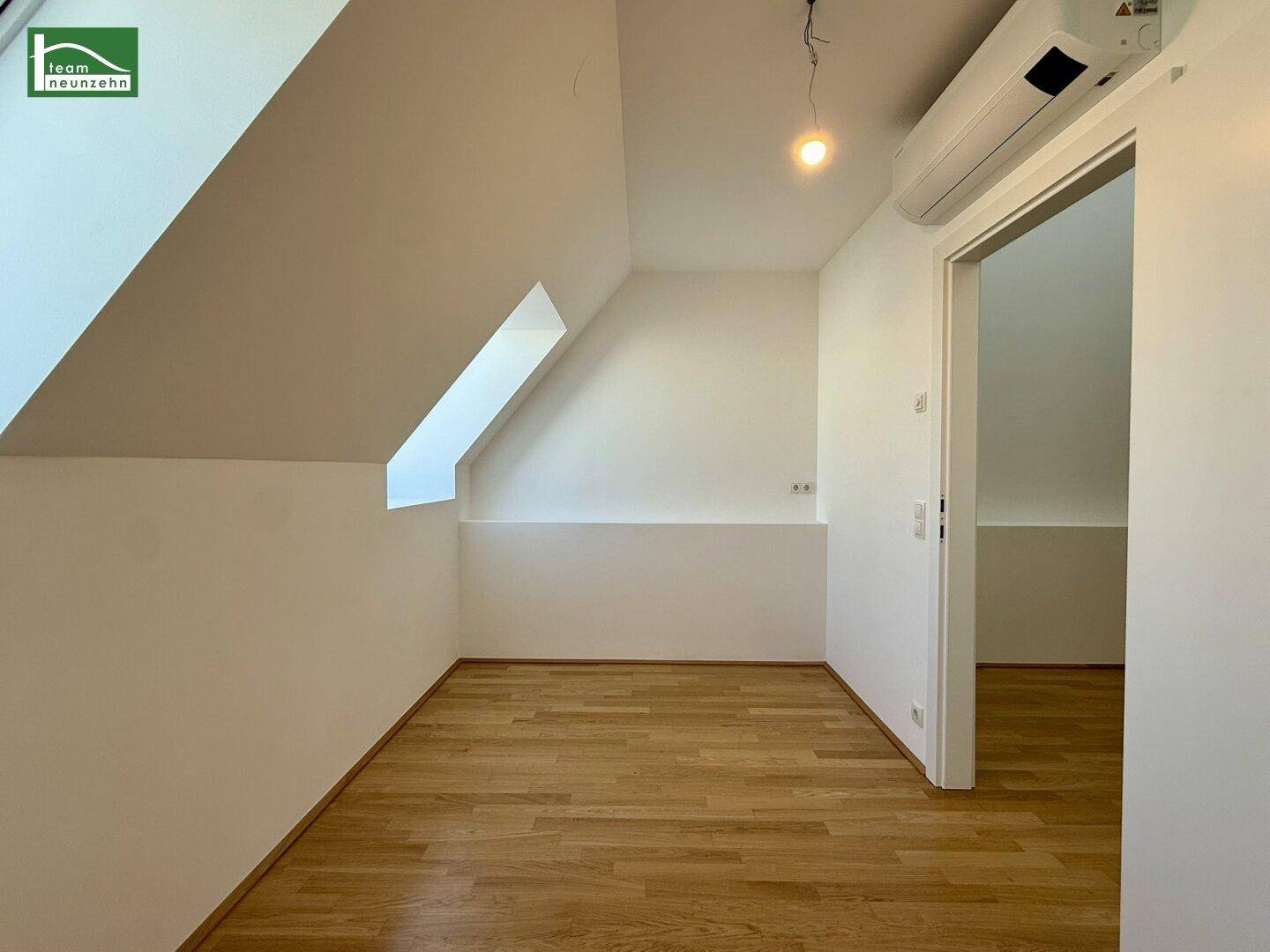 Kleiner, heller Raum im Dachgeschoss mit schrägen Wänden, Dachfenster und Klimaanlage.