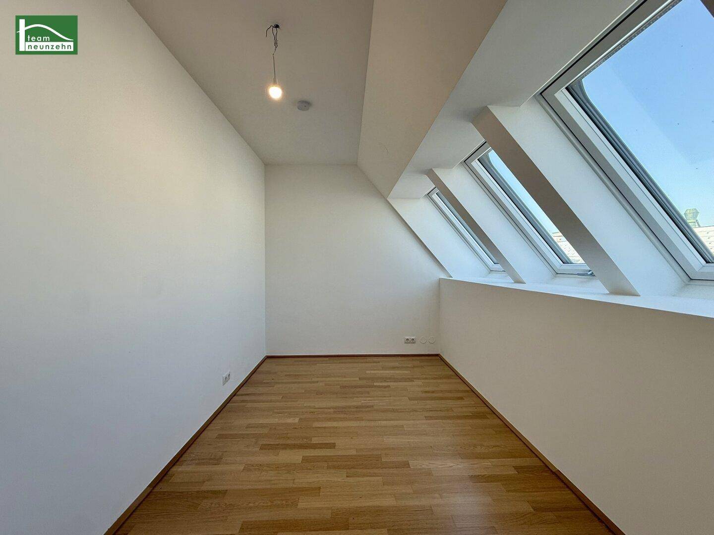 Helles Zimmer im Dachgeschoss mit schrägen Fenstern und Holzboden, ideal als Schlaf- oder Arbeitszimmer.