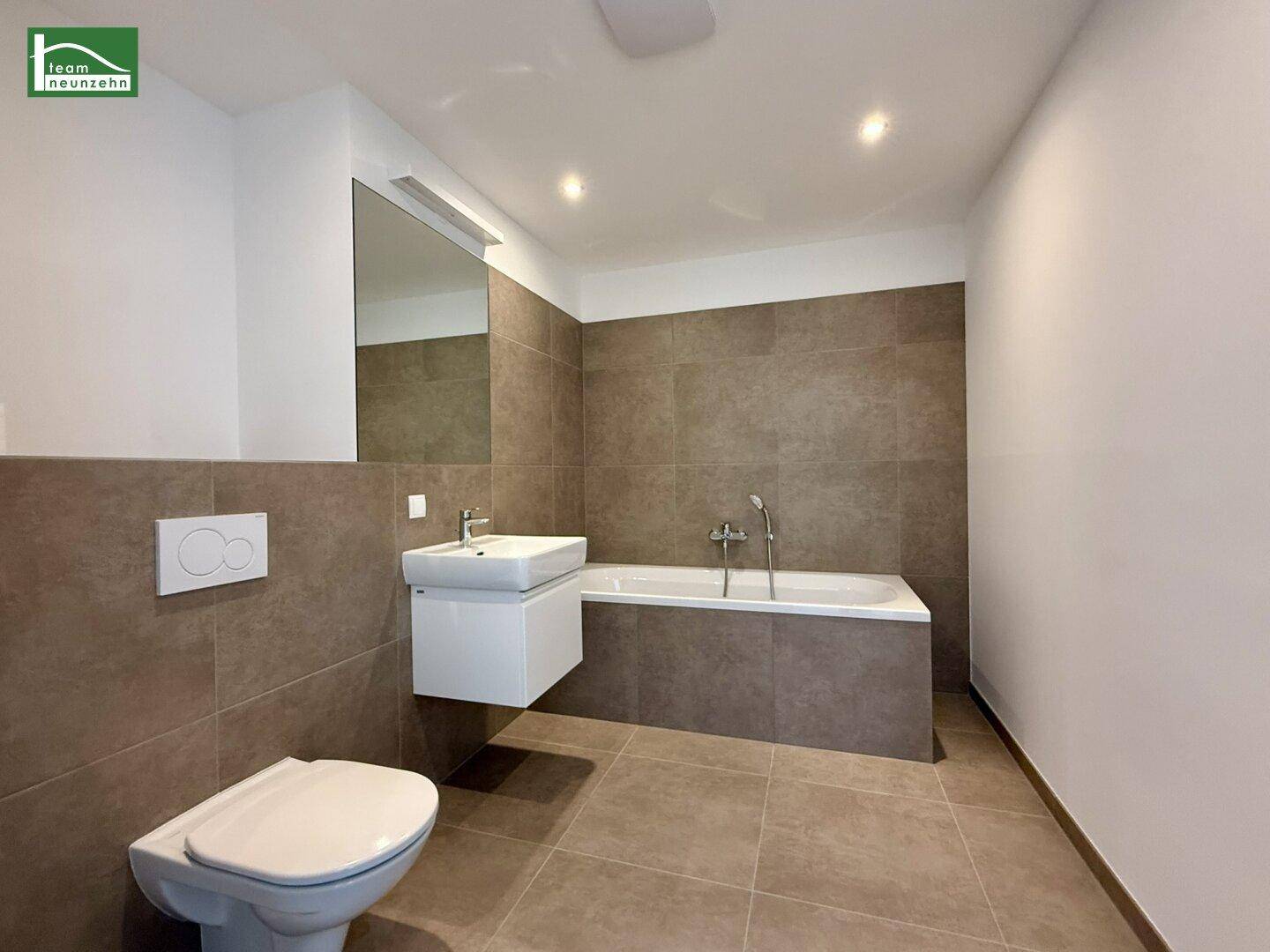 Modernes Badezimmer mit Badewanne, Wand-WC und Waschbecken, ausgestattet mit großen Fliesen.