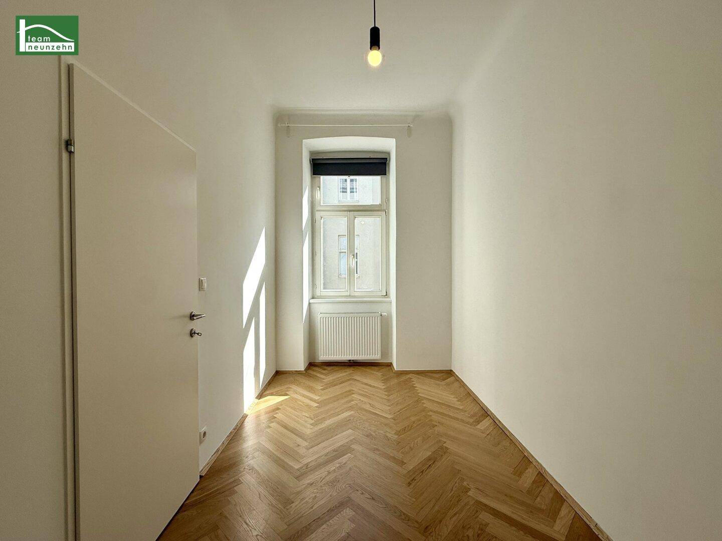 Ruhiges Zimmer mit Fischgrätparkett und weißen Wänden, ausgestattet mit einem Fenster und Rollladen.