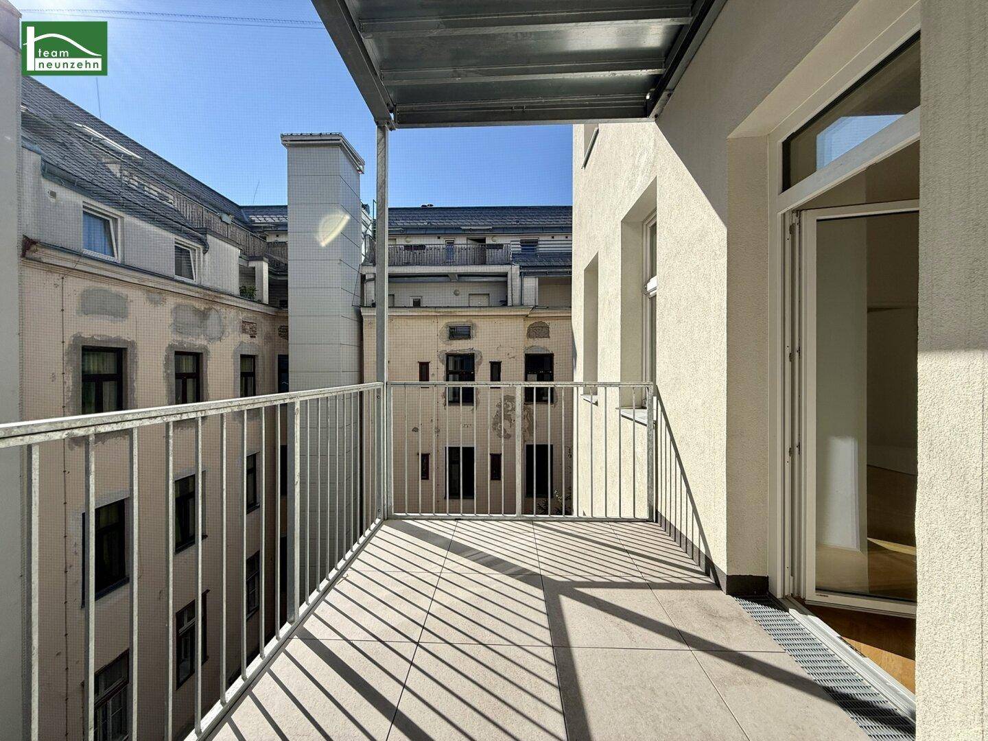 Heller Balkon mit Fliesenboden und Metallgeländer, bietet einen Blick auf den Innenhof der umliegenden Gebäude.