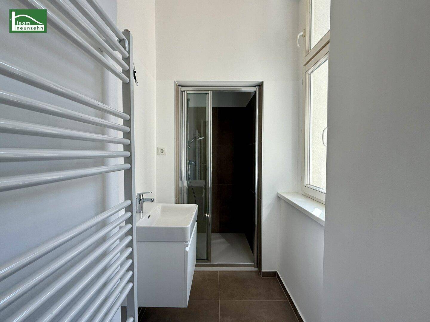 Modernes Badezimmer mit Duschkabine, Einzelwaschbecken, beheiztem Handtuchhalter und Fenster.